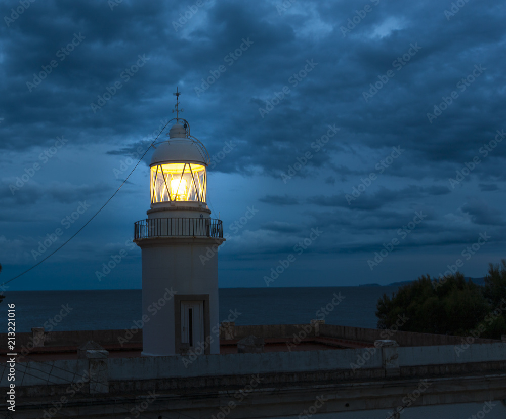 Lighthouse glowing at dark night on coast Spain