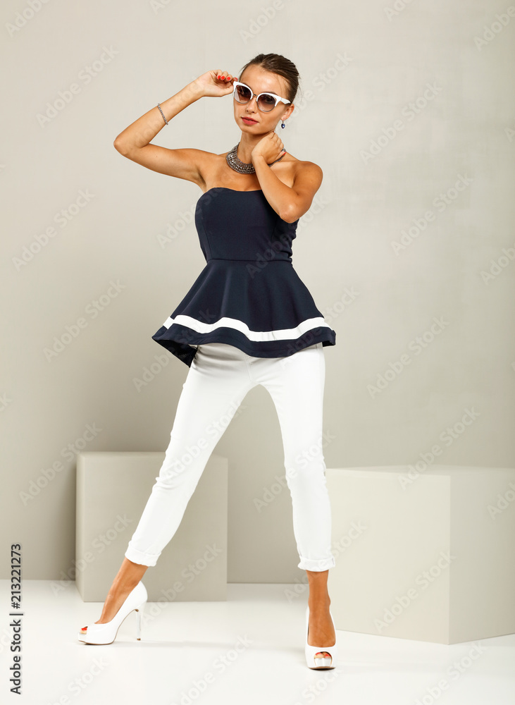 Fototapeta premium Beautiful and attractive model dressed in expensive clothes. White pants, navy blue blouse and high heels. A photo of a fashion shot in the studio.