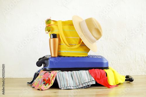 Close up of clothes don't fit in messy fully packed closed suitcase, things sticking out. Blue hard shell luggage. Beach bag, hat, sunglasses. Woman packing for vacation concept. Copy space background