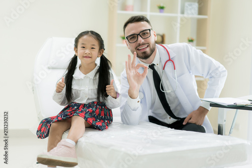 Doctor with cute little girl showing thump up OK signs in hospital. Medicine and health care concept..