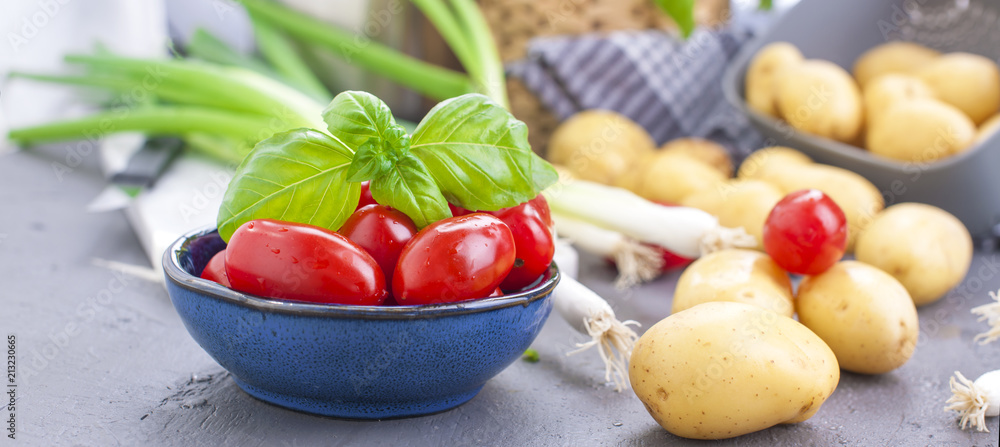 Fresh green onions, young potatoes, cherry tomatoes and green basil. Healthy food and vitamins.Preparation of lunch. Summer seasonal vegetables. Copy space. Banner.