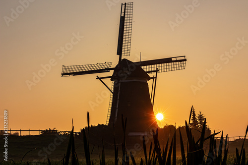 Sun appears behind a windmill in the morning mist