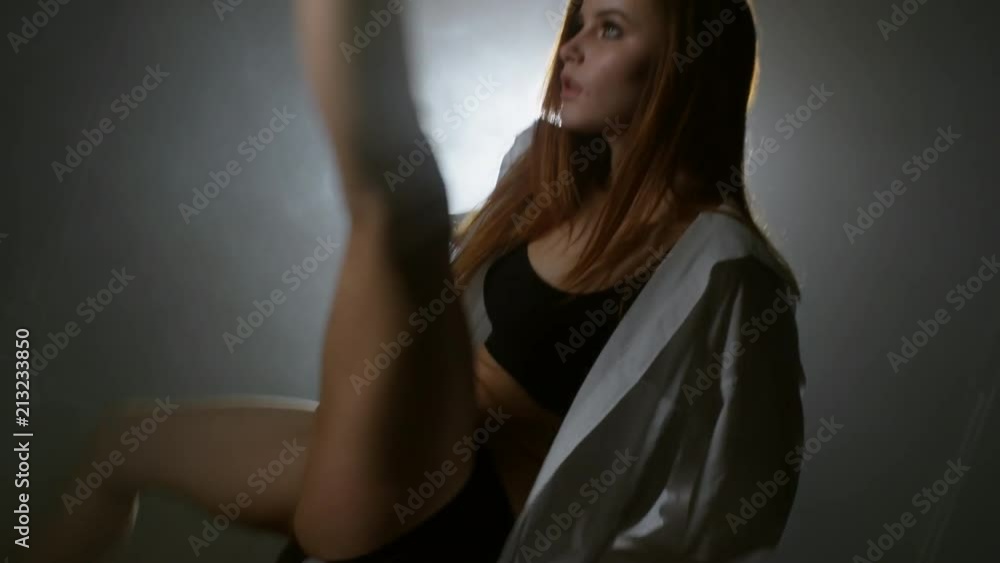 Handheld shot of sexy young woman in shirt and high heel shoes chair dancing and moving elegantly before camera in dark studio filled with fog Handheld shot of sexy young woman in shirt and high heel shoes chair dancing and moving elegantly before camera in dark studio filled with fog