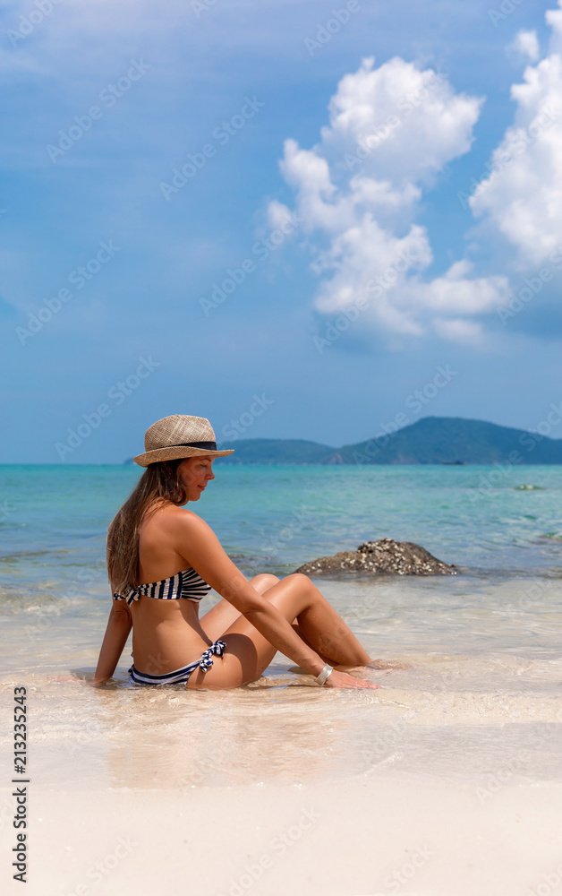 Young woman in straw hat sits on the white beach near sea Young woman in straw hat sits on the white beach near sea