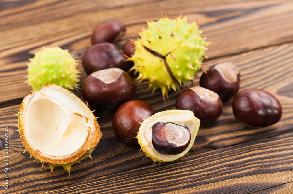 Heap of green prickly and brown smooth chestnuts on old wooden rustic brown table Heap of green prickly and brown smooth chestnuts on old wooden rustic brown table