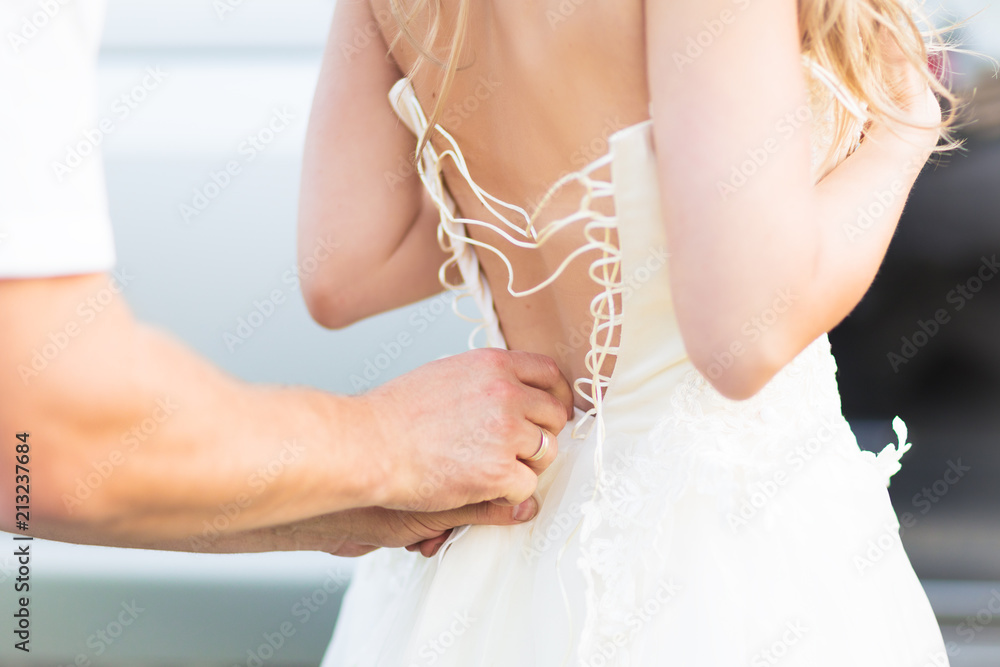 Closeup photo of man tying up beautiful bride wedding dress