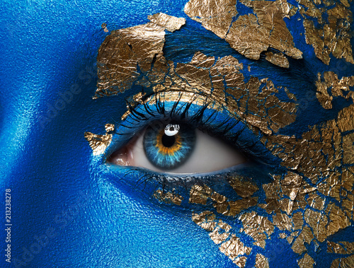 Artistic make-up and body art theme: portrait of a beautiful young girl model with blue make-up all over the body with gold foil for make-up