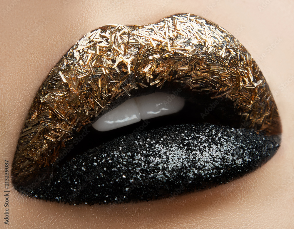 Obraz premium Macro and close-up creative make-up theme: beautiful female lips with black and gold lipstick and sparkles, retouched photo