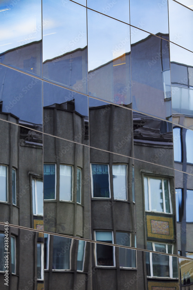 Fragmented facade of old building reflected in windows of modern office building