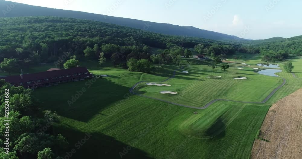 Aerial camera moving to the right showing a large lodge on a green golf course surrounded by forest. Aerial camera moving to the right showing a large lodge on a green golf course surrounded by forest.
