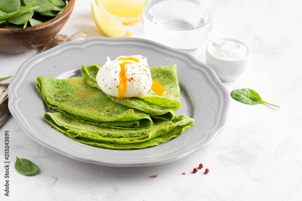 Green thin pancakes with spinach, poached egg, sour cream, lemon and aromatic herbs, delicious healthy food Green thin pancakes with spinach, poached egg, sour cream, lemon and aromatic herbs, delicious healthy food