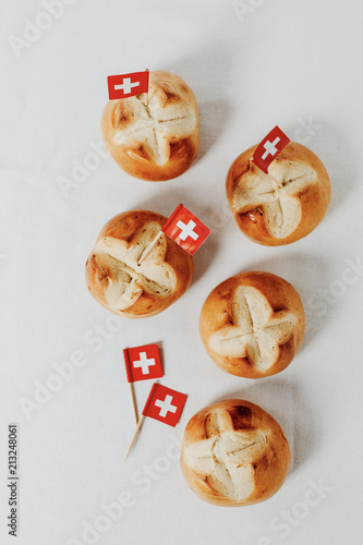 Swiss bread buns called in German 1. Augustweggen baked in Switzerland to celebrate Swiss National Day on August 1st. Swiss flag with white cross on red background.  White background, isolated.