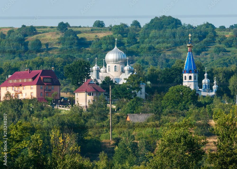 The tops of church temples with colorful roofs and domes against the background of green mountain slopes