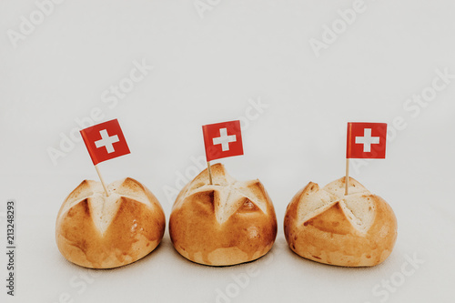 Swiss bread buns called in German 1. Augustweggen baked in Switzerland to celebrate Swiss National Day on August 1st. Swiss flag with white cross on red background.  White background, isolated.