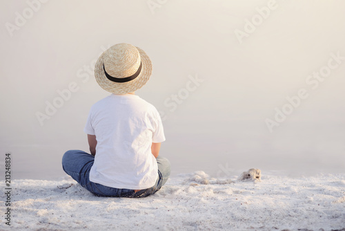 sad and pensive boy sitting on the beach, rear view