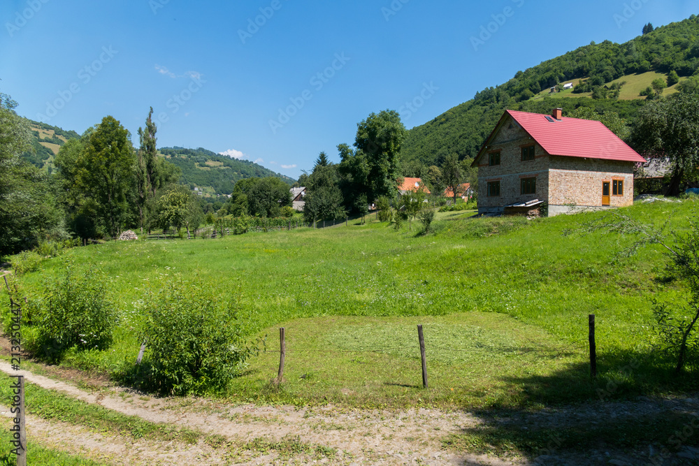 A rural road running next to the yard with a green lawn and a house standing in the depths on the hill. A rural road running next to the yard with a green lawn and a house standing in the depths on the hill.