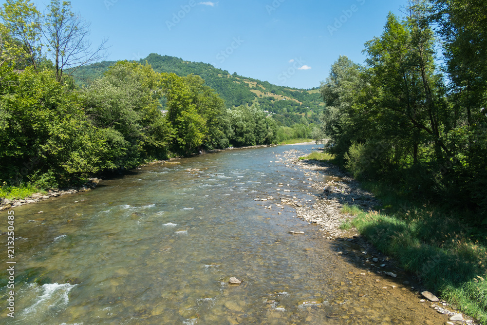 A mountain shallow river with clear water and a bottom filled with stones flowing among A mountain shallow river with clear water and a bottom filled with stones flowing among