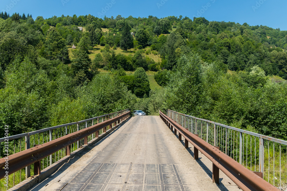 Old car bridge with rusty railing against the background of a green slope with trees