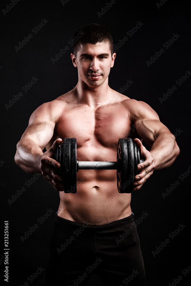 Muscular bodybuilder guy doing exercises with dumbbell over black background