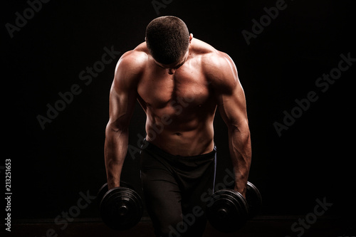 Muscular bodybuilder guy doing exercises with dumbbell over black background