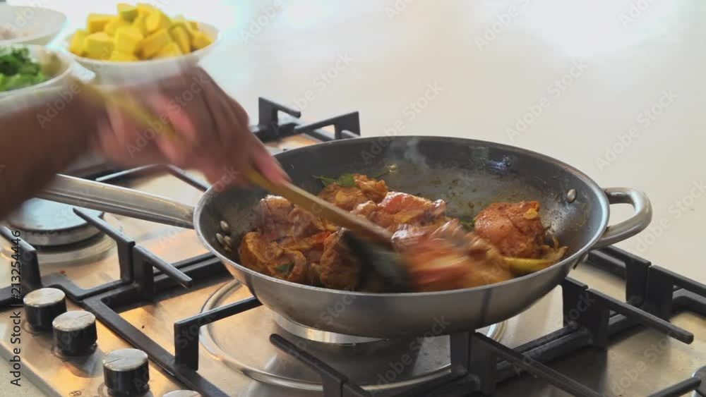 Close up of a frying pan as a Sri Lankan chef adds chicken to a sri
