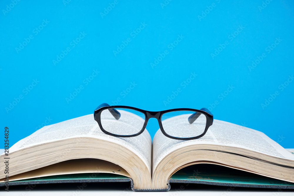 Education concept. An old book, eyeglasses over blue background Education concept. An old book, eyeglasses over blue background