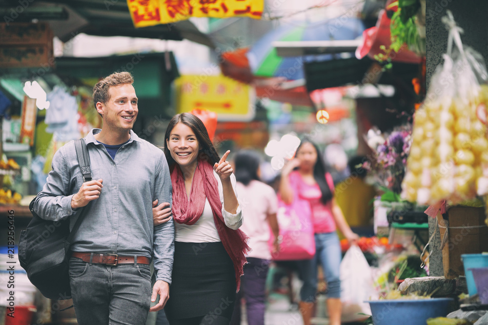 Naklejka premium Interracial para turystów chodzących na zakupy na rynku chińskim w Hongkongu w Chinach. Młodzi ludzie podróżujący po Azji patrząc na lokalne uliczne jedzenie. Azjatka, kaukaski mężczyzna.