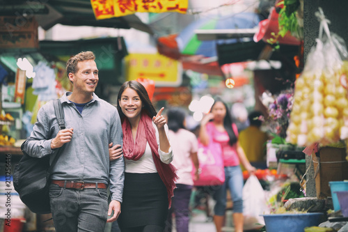 Interracial couple tourists walking shopping in chinese market in Hong Kong, China. Young people traveling in Asia looking at local street food. Asian woman, Caucasian man. photo