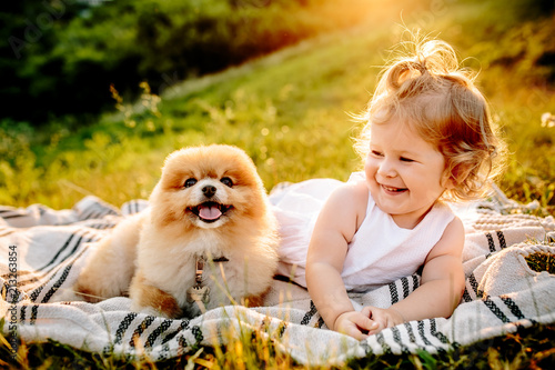 Little girl and pets. The girl and a dog lying on a blanket on a green park. Sunset time. Pedigree dogs Spitz. Funny animals. Outdoor picnic. © matilda553