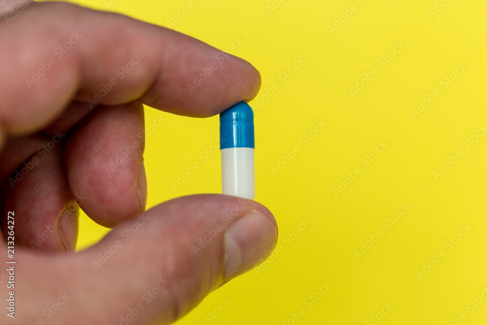 Hand holding drugs pills capsule on yellow background Hand holding drugs pills capsule on yellow background
