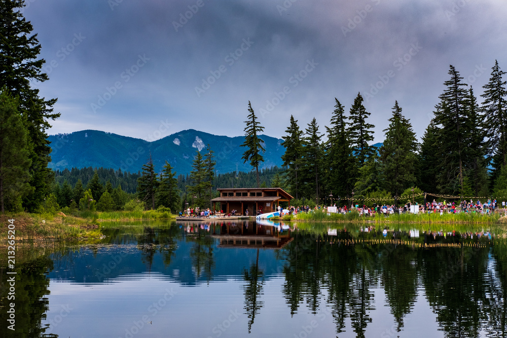 Fototapeta premium A party at a building on a lake with reflections and mountains in the background