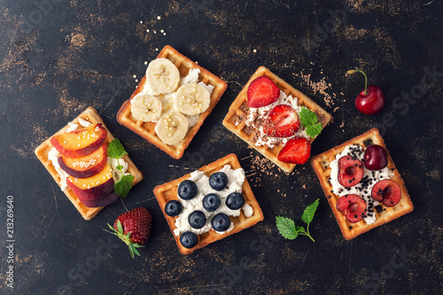 Belgian waffles with blueberries,strawberries,peaches, cherries and banana. Homemade waffles on a dark rustic background. The view from the top,flat lay.