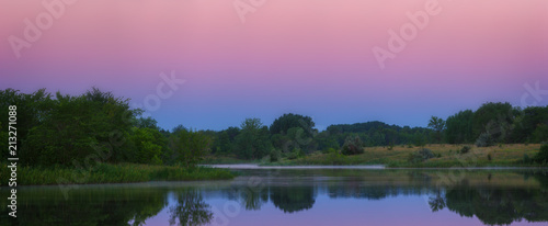 The morning sky is reflected in the smooth surface of the lake. Panoramic view of the landscape in summer in Russia.