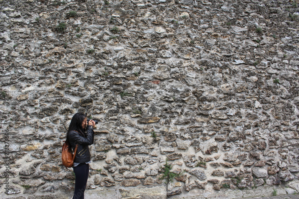 YOUNG WOMAN TAKING PHOTOGRAPHS, STONE WALL BACKGROUND