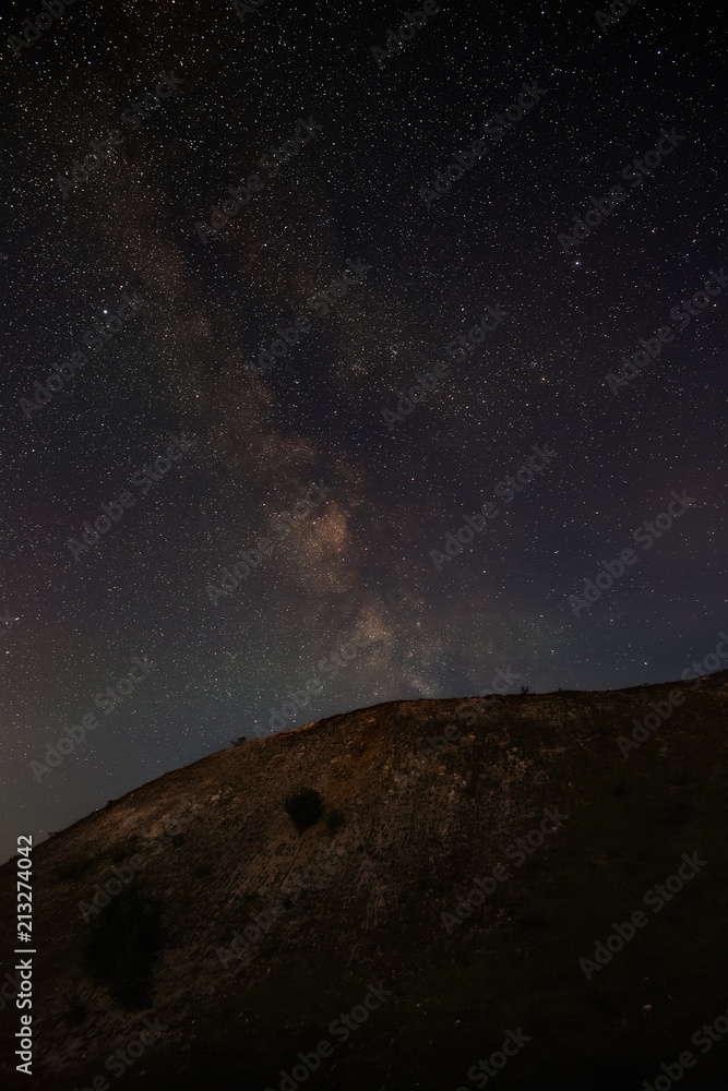 The stars of the Milky Way in the night sky over a hilly landscape. The cosmic space is photographed on a long exposure.