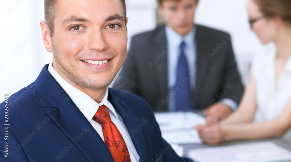 Portrait of cheerful smiling business man against a group of business people at a meeting Portrait of cheerful smiling business man against a group of business people at a meeting