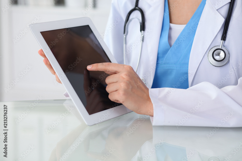 Female doctor using tablet computer while sitting at the workplace, close-up of hands. Medicine, healthcare and help concept Female doctor using tablet computer while sitting at the workplace, close-up of hands. Medicine, healthcare and help concept