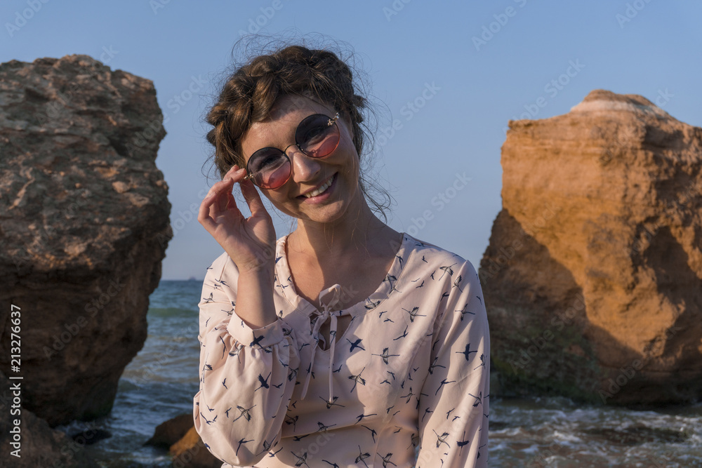 Fototapeta premium Adorable Caucasian Brunette girl in Light Dress and sunglasses Enjoying at the Seacoast at Sunrise time.