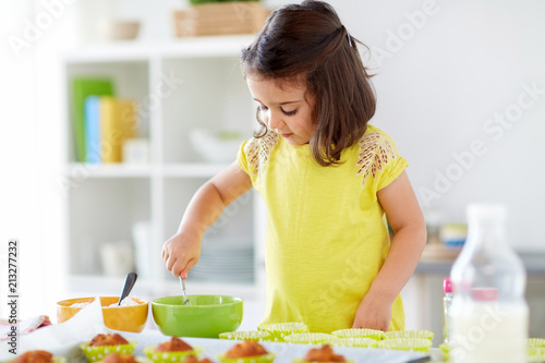 family, cooking, baking and people concept - little girl making batter for muffins or cupcakes at home kitchen