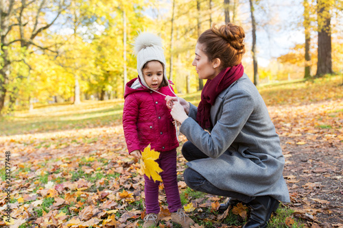 family, season and people concept - happy mother and little daughter with autumn leaves at park