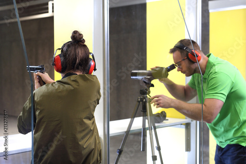 Nauka strzelania. Kobieta strzela z broni na strzelnicy pod okiem instruktora.