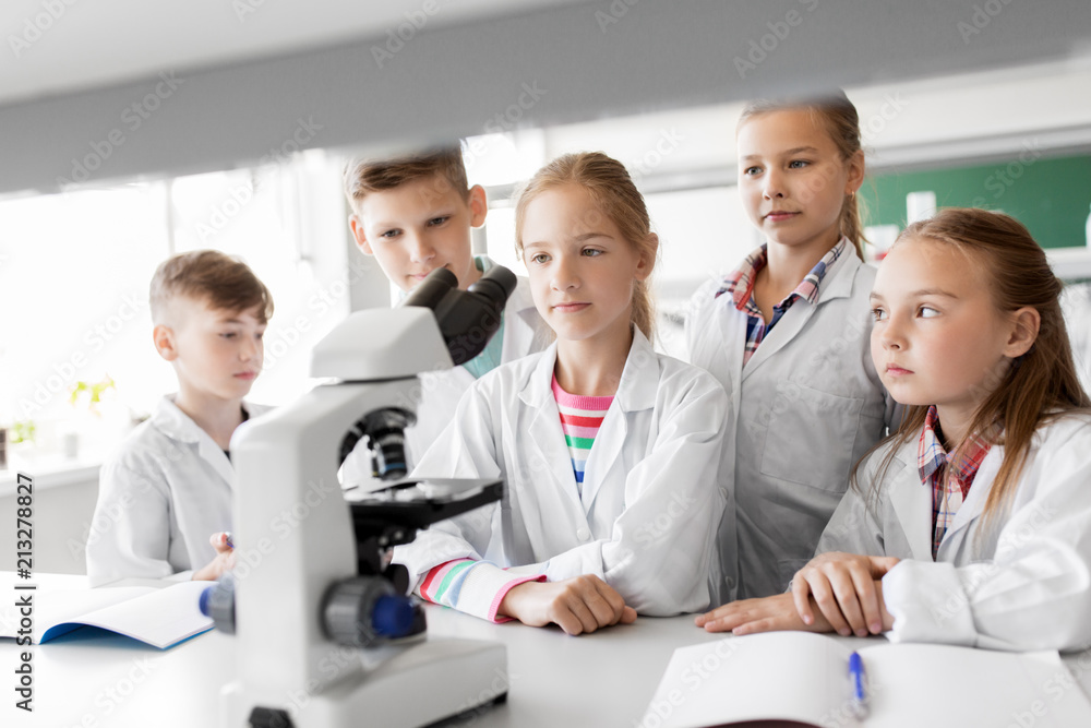education, science and children concept - kids or students with microscope studying biology at school laboratory