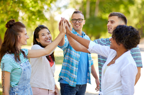 success, friendship and international concept - group of happy smiling friends making high five in park