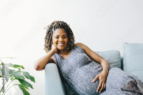 Portrait of pregnant woman leaning on sofa against wall at home