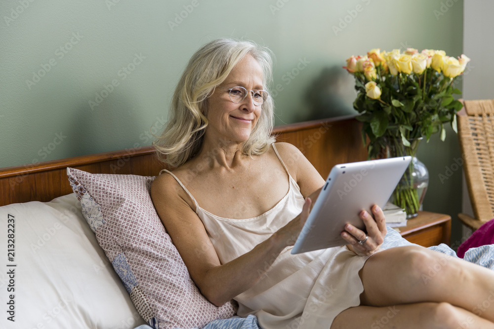 © Cavan Images - Smiling senior woman using tablet computer on bed at home © Cavan Images - Smiling senior woman using tablet computer on bed at home