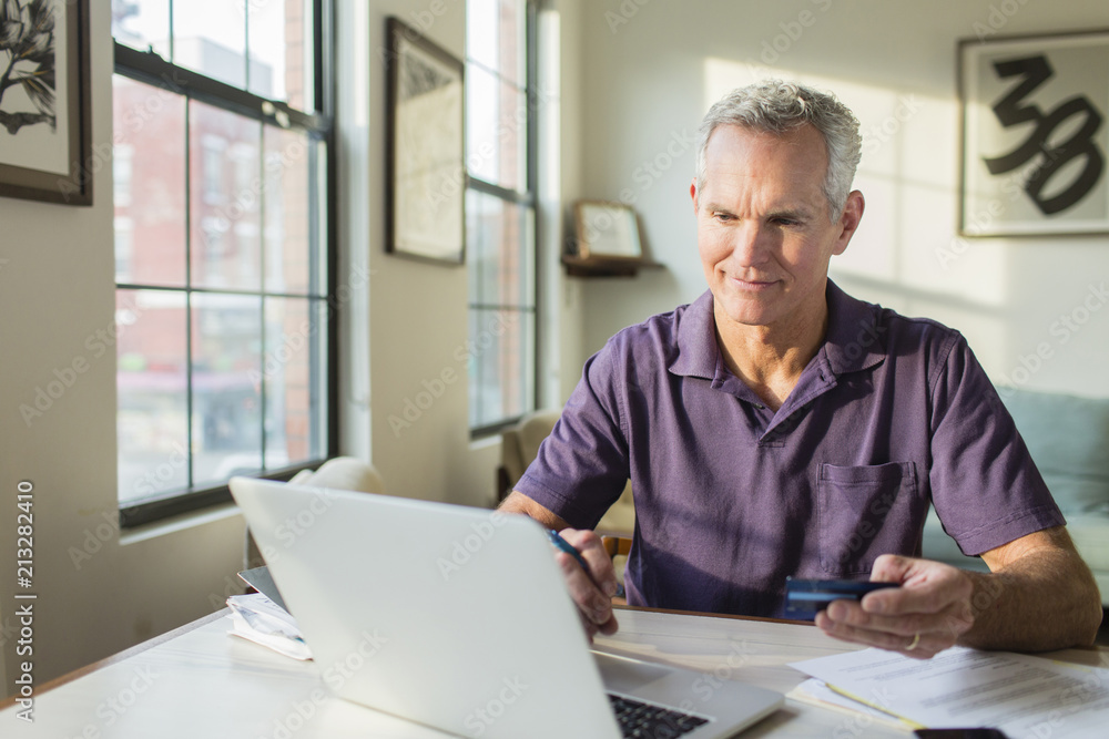 Mature man using laptop computer while paying bills at home Mature man using laptop computer while paying bills at home