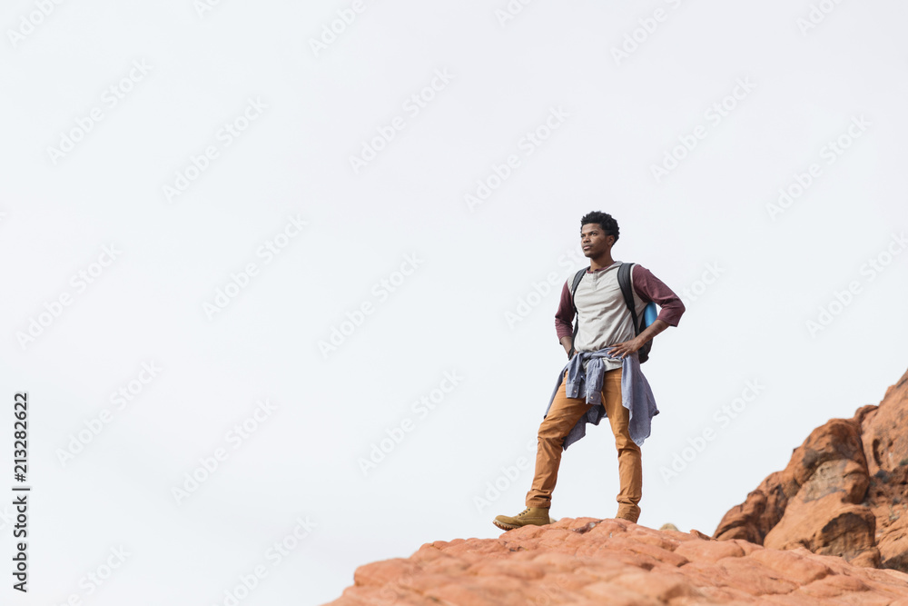 Low angle view of man with hands on hip looking away while standing on rock formation against clear sky Low angle view of man with hands on hip looking away while standing on rock formation against clear sky