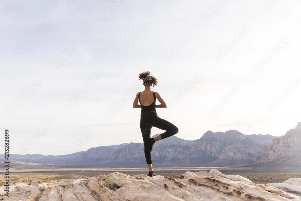 Rear view of woman meditating while standing on rock formation against sky Rear view of woman meditating while standing on rock formation against sky