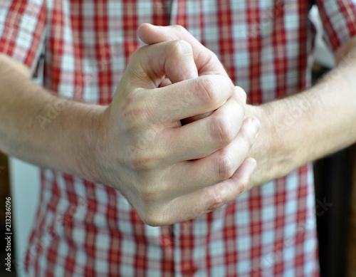 A man with a red shirt in plaid, cracking his knuckles of the hand, front view, selective focus, close up