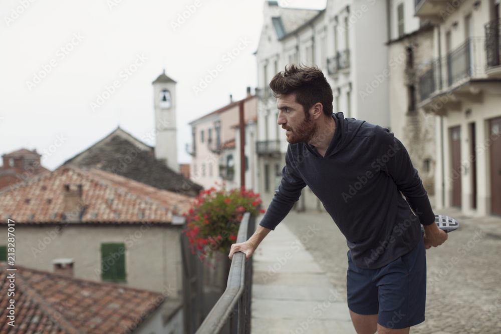 Confident man stretching leg while exercising by railing in town Confident man stretching leg while exercising by railing in town